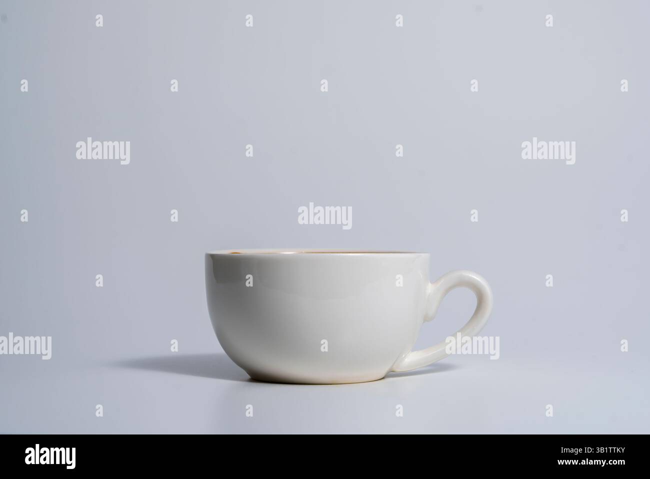 Una tazza in ceramica bianca semplice con manico posizionato su una superficie leggera, che emette un'ombra morbida, catturata in una composizione minimalista e pulita. Foto Stock