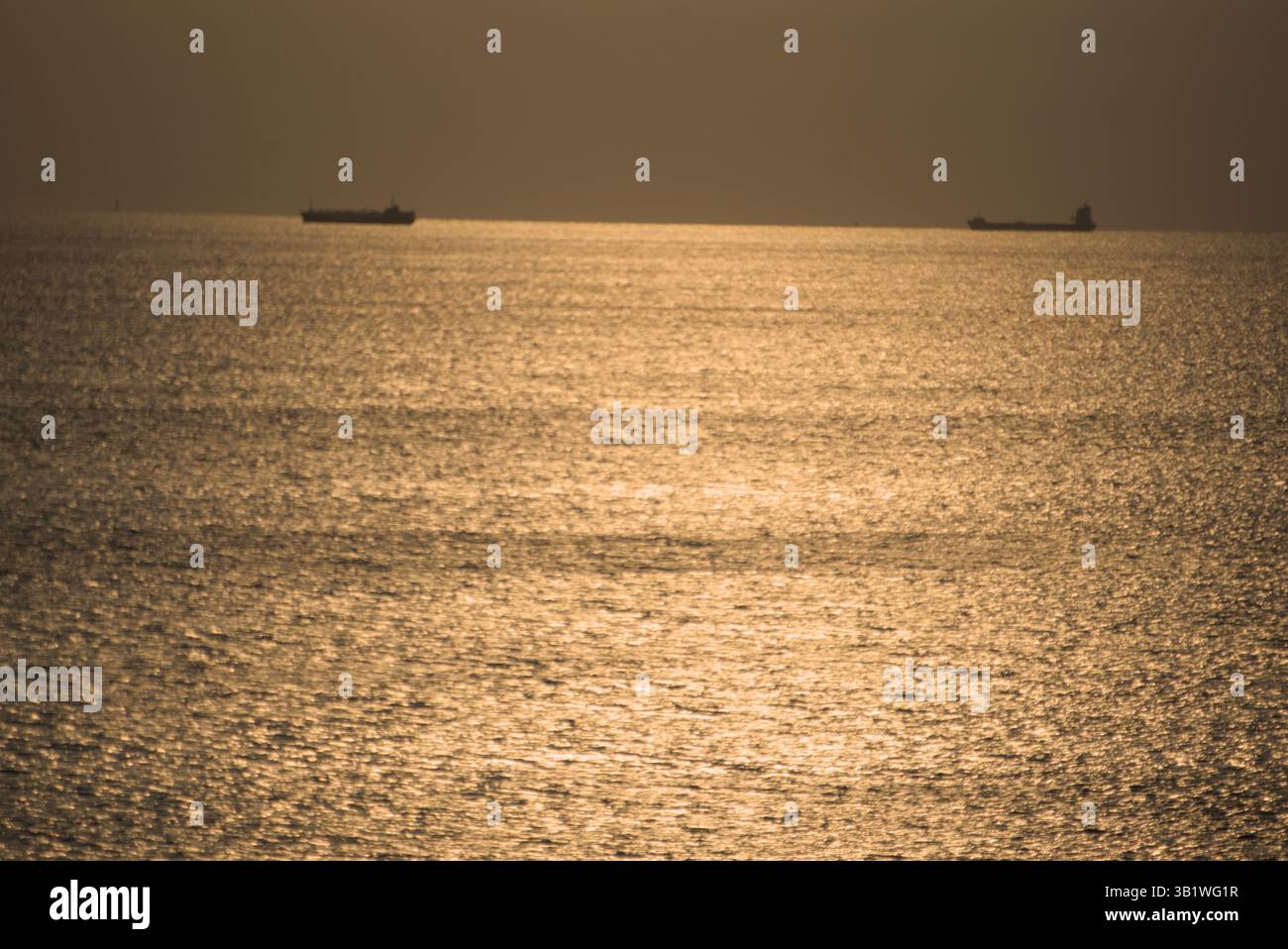 La luce dorata della sera si riflette sul mare mentre due navi da carico modellano l'orizzonte in un tranquillo paesaggio marino. Salou, Spagna Foto Stock