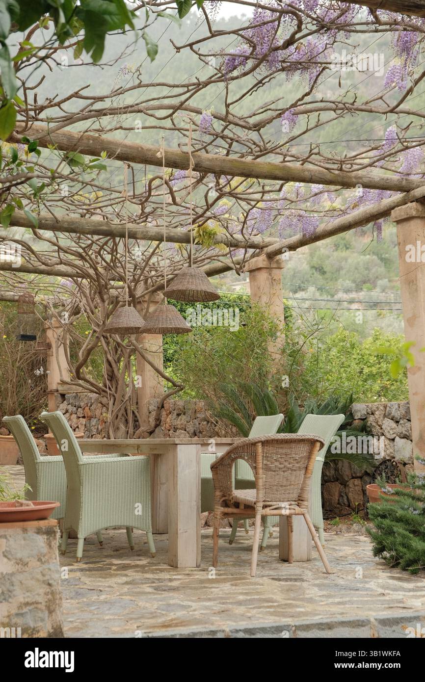 Accogliente terrazza arredata con mobili da giardino bianchi sotto alberi fioriti in un giardino mediterraneo con ambiente naturale. Foto Stock