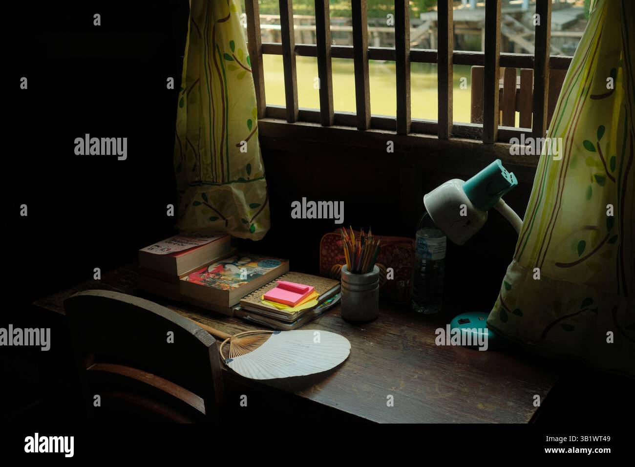 Angolo lettura vintage vicino a una finestra con libri, lampada e arredamento in vecchio stile a Ko Kret, Thailandia. Foto Stock