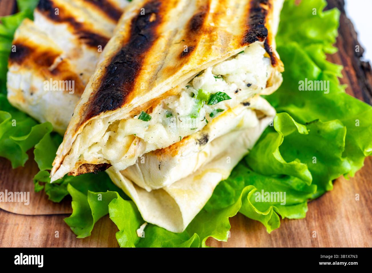 Un involtino appena grigliato è caratterizzato da teneri pollo ed erbe aromatiche, annidati tra strati di morbida tortilla. Poggia su un vivace letto verde di lattuga croccante, Foto Stock