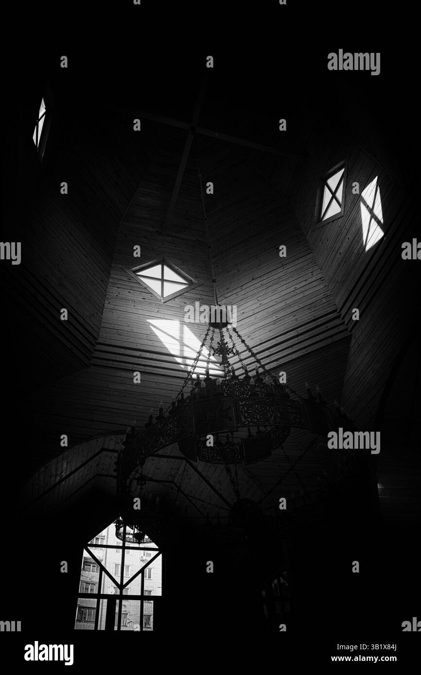 Immagine in bianco e nero moodia di una volta a soffitto di una chiesa in legno con un lampadario decorato. La luce dalle finestre geometriche crea ombre drammatiche, enfasi Foto Stock Immagine in bianco e nero moodia di una volta a soffitto di una chiesa in legno con un lampadario decorato. La luce dalle finestre geometriche crea ombre drammatiche, enfasi Foto Stock