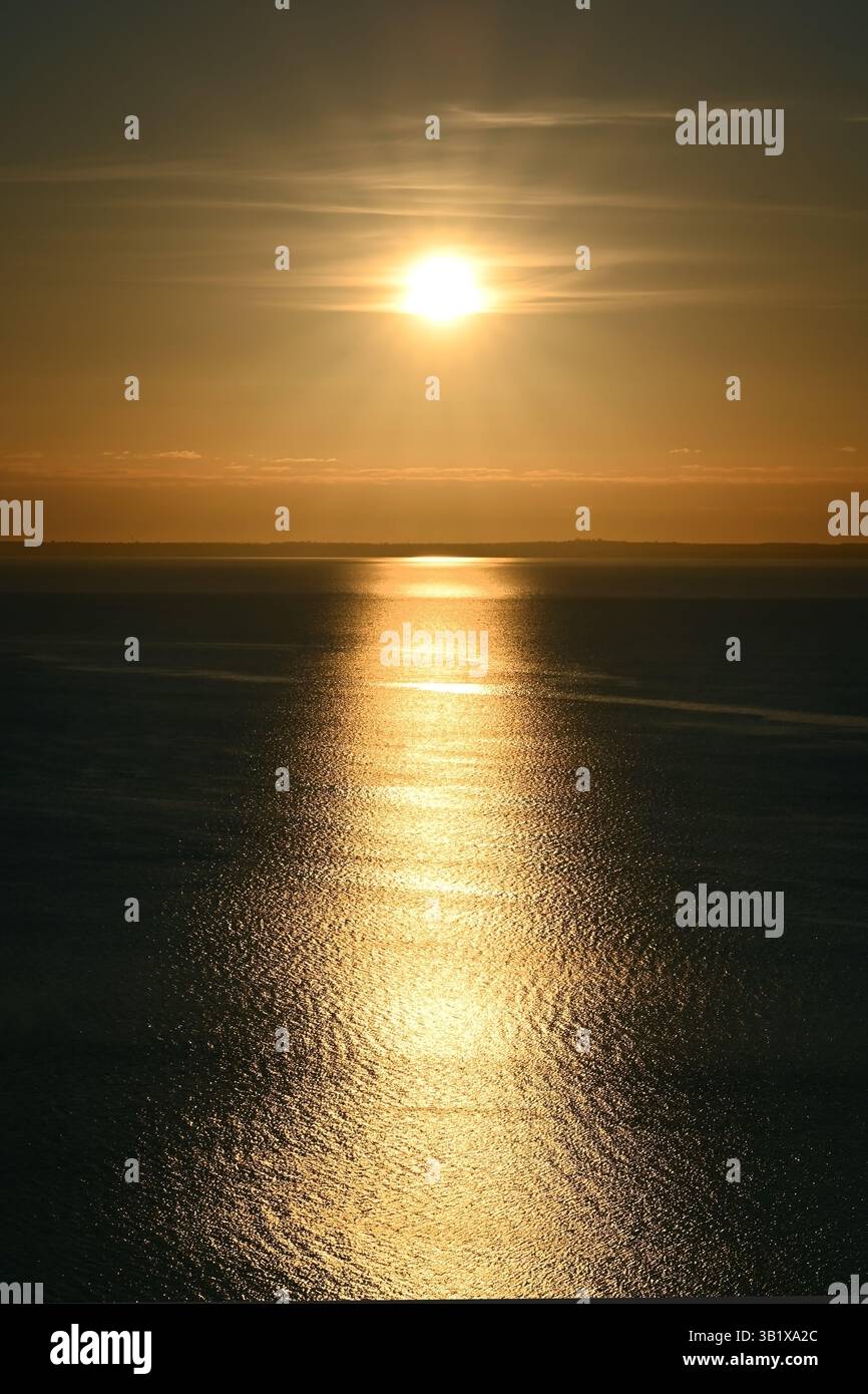 Il sole si riflette sulla tranquilla superficie dell'acqua con sottili increspature all'alba sul lago Balaton, in formato verticale Foto Stock
