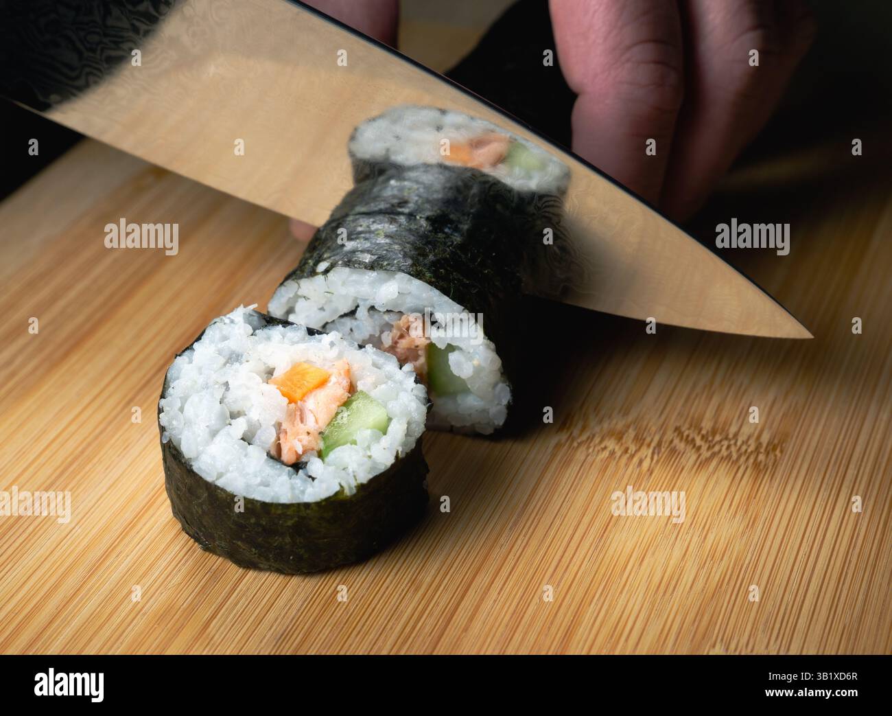 Una persona sta tagliando un sushi roll con un coltello. Il sushi roll è composto da riso, salmone e verdure. Il coltello è posizionato al centro dello sterzo Foto Stock