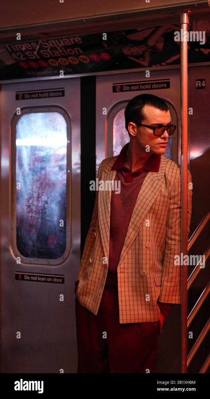 Una persona che indossa un blazer a quadri beige e pantaloni color marrone si trova in una macchina della metropolitana. Sopra è visibile la segnaletica della 42nd Street Station di Times Square. La colomba Foto Stock