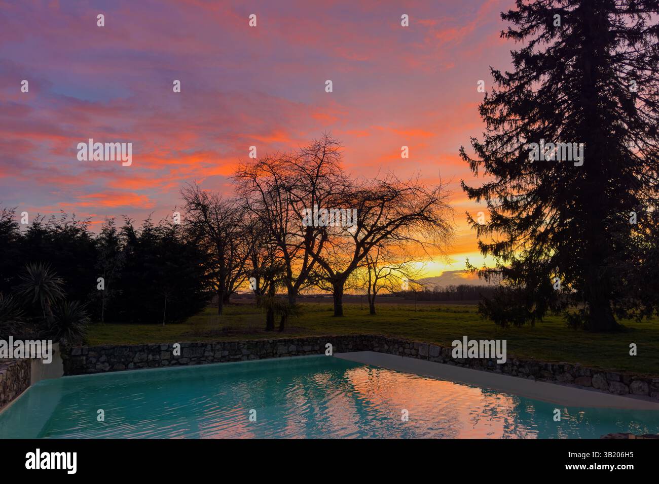 splendido tramonto rosso nuvoloso sulla campagna, piscina in primo piano Foto Stock