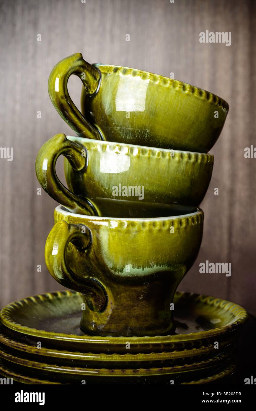 Un vecchio set vintage per tè e caffè con glassa. Ceramica retrò con tre tazze e piattini di colore verde autunnale su sfondo in legno Foto Stock