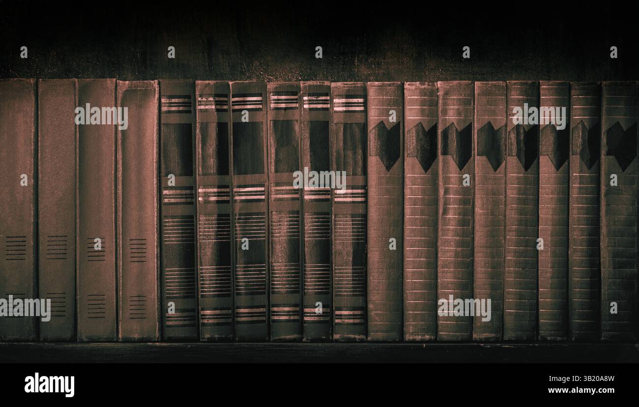 Vecchi libri rilegati in pelle su scaffale in legno vintage in una biblioteca di storia e scienza su sfondo marrone scuro Foto Stock