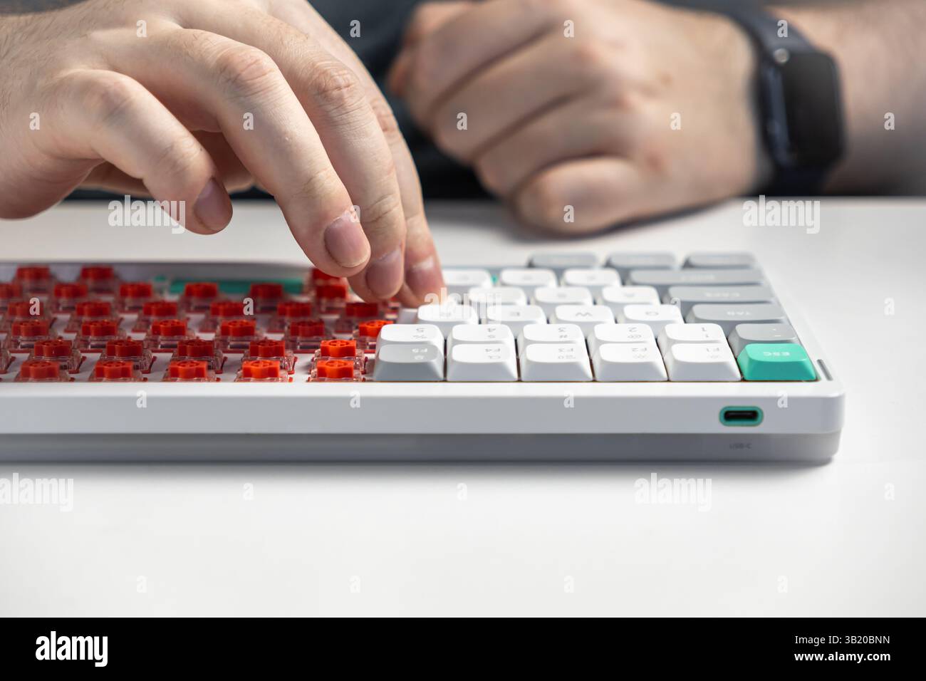 Vista ravvicinata delle mani che posizionano i cappucci bianchi sugli interruttori rossi a basso profilo su una tastiera meccanica bianca che illustra il processo di assemblaggio tecnico e Foto Stock
