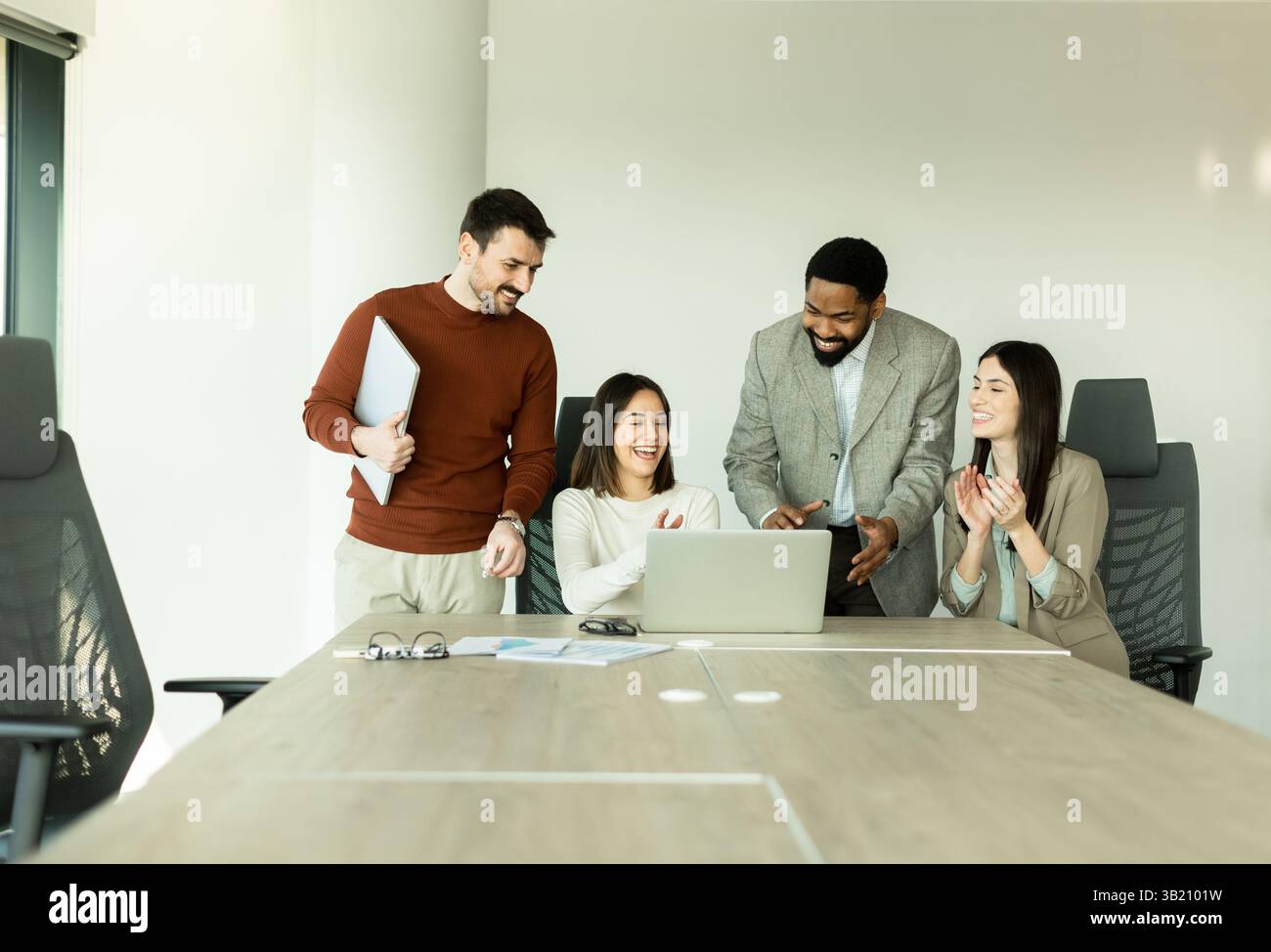 Un gruppo eterogeneo di professionisti si impegna in una sessione di brainstorming dinamica attorno a un tavolo da conferenza, condividendo idee mentre interagiscono con i laptop e Foto Stock
