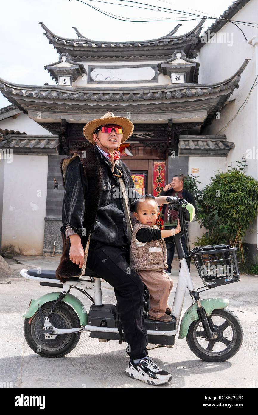 (250427) -- KUNMING, 27 aprile 2025 (Xinhua) -- Yang Siyun, un discendente di operatori locali di treni a cavallo, cavalca una bicicletta elettrica con suo figlio nel villaggio di Sideng della città di Shaxi, nella contea di Jianchuan, nella provincia di Yunnan, nella Cina sud-occidentale, 19 aprile 2025. Una remota città nella contea di Jianchuan, Shaxi era un tempo un importante centro commerciale per tè, erbe, sete e sale sull'antica Tea Horse Road, una via commerciale che risale alla dinastia Tang (618-907). Tuttavia, il centro commerciale alla fine del XIX secolo vide un declino perché era lontano dalle moderne strade arteriose emergenti e da altri mezzi di trasporto Foto Stock