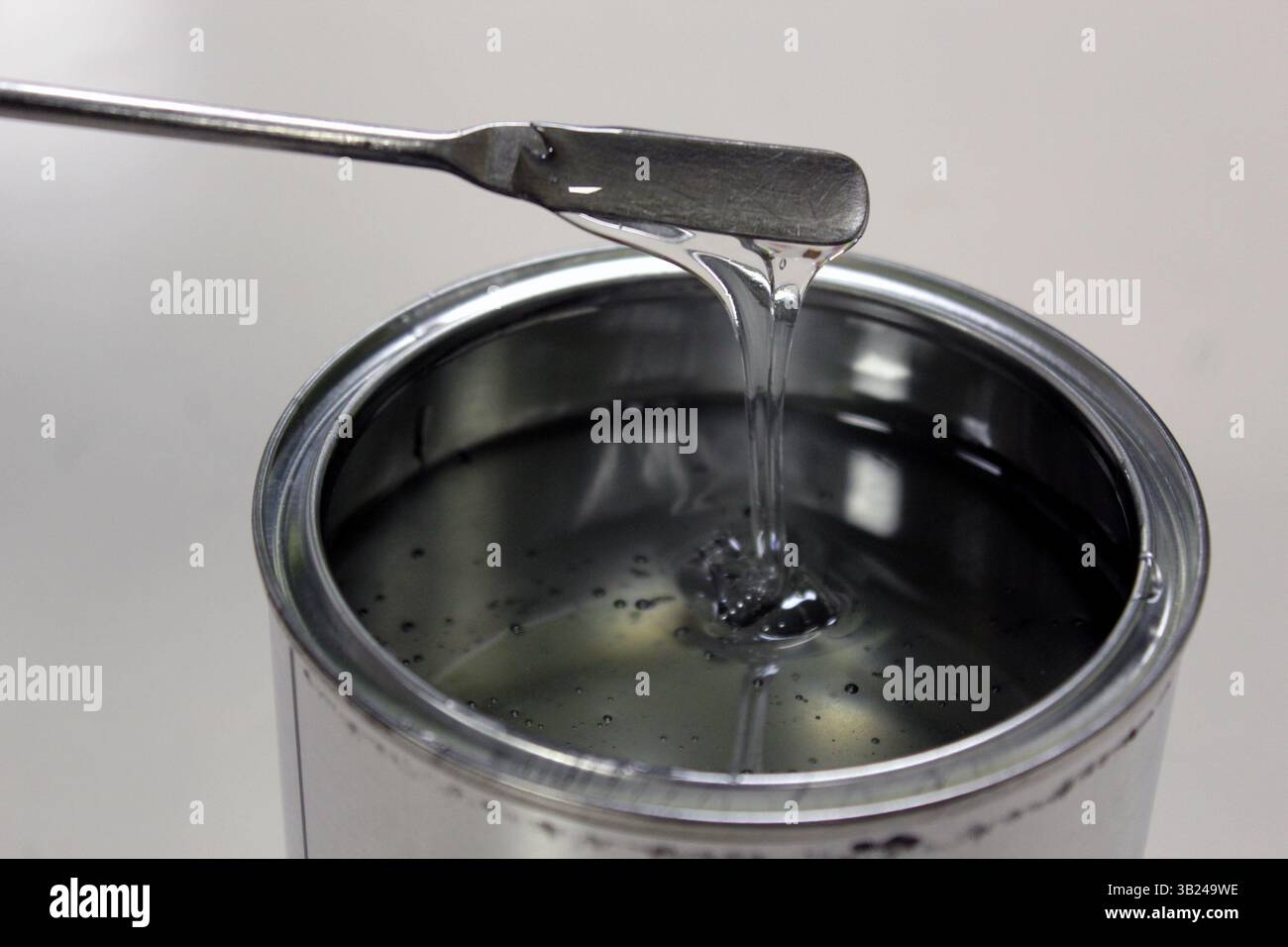 Tecnico che pesa resina epossidica trasparente per una vernice in lattina su bilancia mediante spatola su sfondo bianco Foto Stock