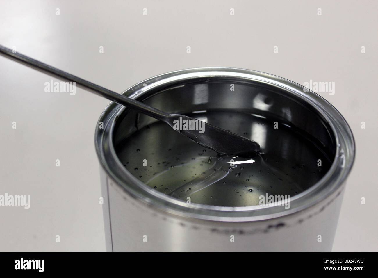 Tecnico che pesa resina epossidica trasparente per una vernice in lattina su bilancia mediante spatola su sfondo bianco Foto Stock