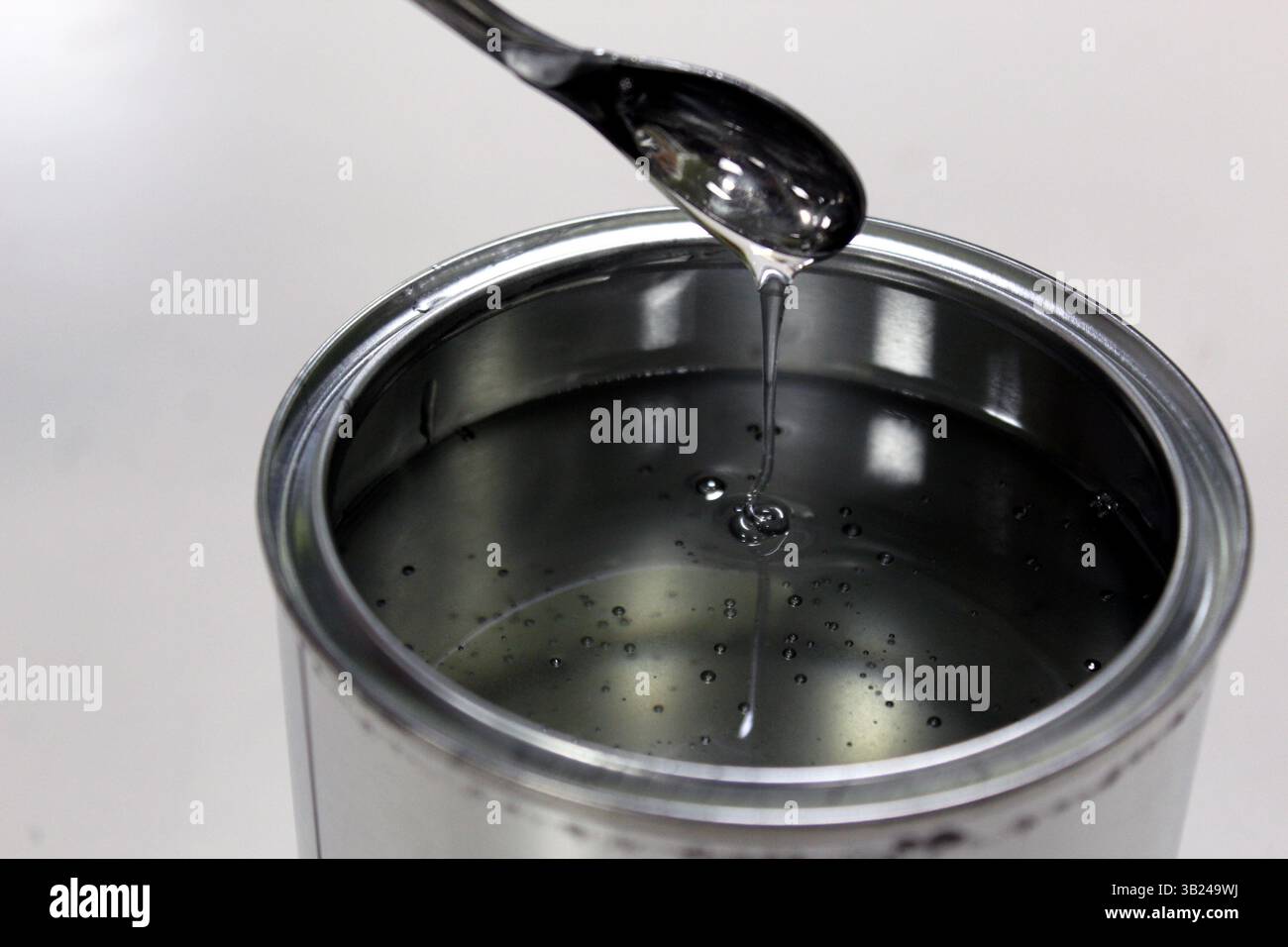 Tecnico che pesa resina epossidica trasparente per una vernice in lattina su bilancia mediante spatola su sfondo bianco Foto Stock