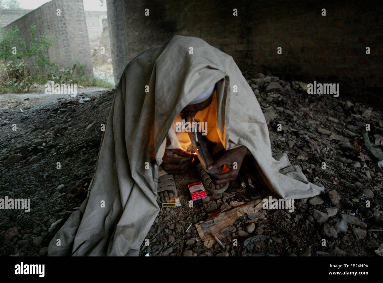 9 febbraio 2009 - Peshawar, Pakistan - Un uomo si copre di una coperta per impedire al vento di colpire la fiamma che usa per accendere il tubo dell'eroina. La maggior parte dei tossicodipendenti fuma fumi di polvere di eroina in un liquido da foglia d'argento con una corrispondenza al calore. Migliaia di eroine tossicodipendenti vivono sotto i ponti di peshawar, Pakistan occidentale. La maggior parte di loro sta rubando per acquistare droga, che è molto economica e disponibile per 1 euro per colpo dall'afghanistan. (Immagine di credito: © Koene/ZUMAPRESS.com) Foto Stock