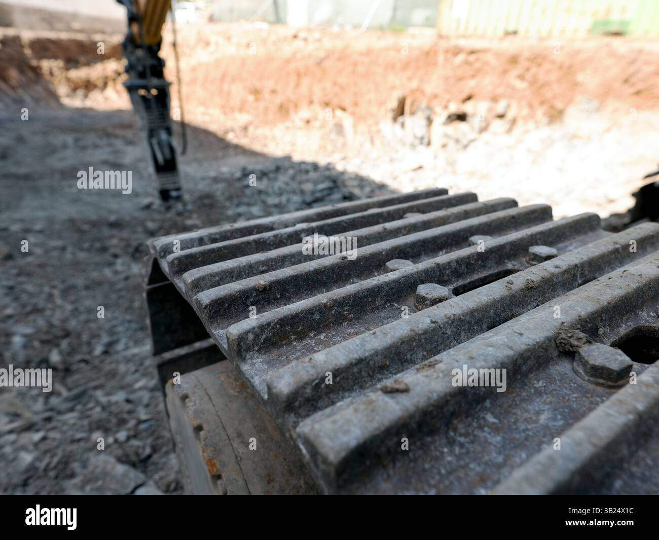 Veicolo cingolato pesante in cantiere con martello idraulico sfocato sullo sfondo polveroso. Foto Stock