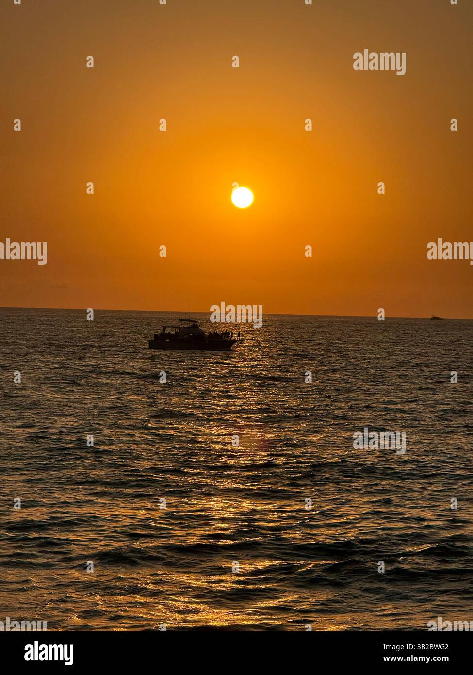 Un tramonto ardente illumina l'oceano mentre una barca naviga attraverso le acque dorate, catturando la magia del momento. - Immagine stock catturata con smartphone