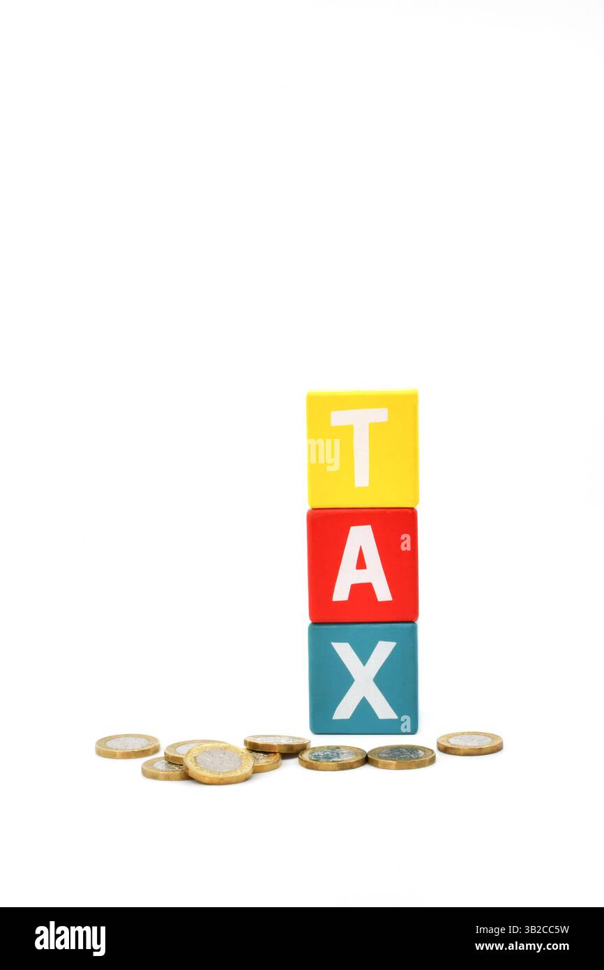 Monete inglesi da una sterlina davanti a blocchi di legno colorati che scrivono la parola Tax isolate su un semplice sfondo bianco Foto Stock