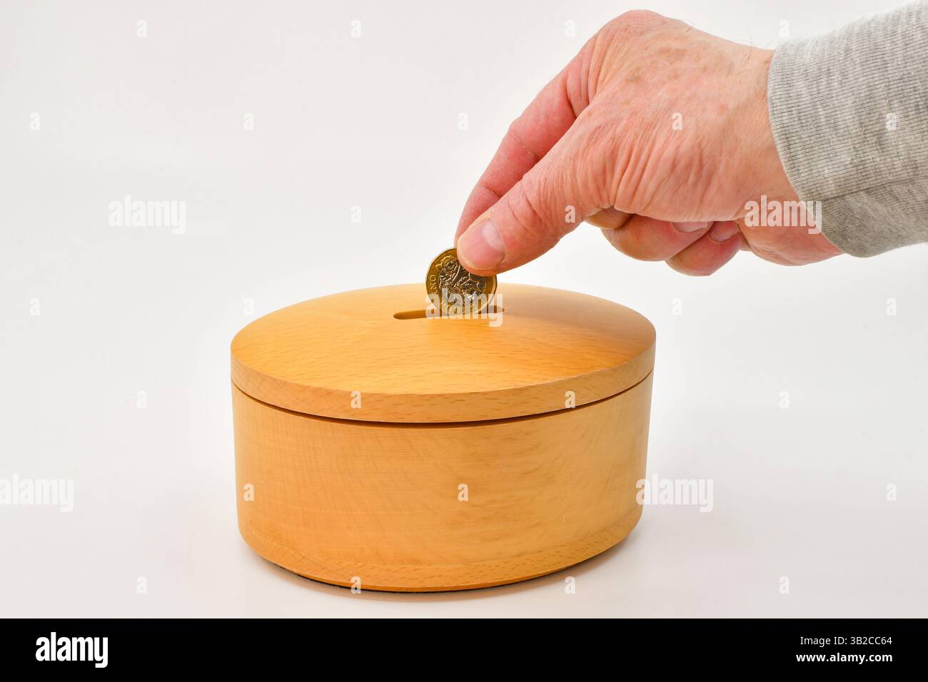 Una moneta da una sterlina da mettere nella fessura di una cassetta di legno. Concetto di salvataggio. Foto Stock