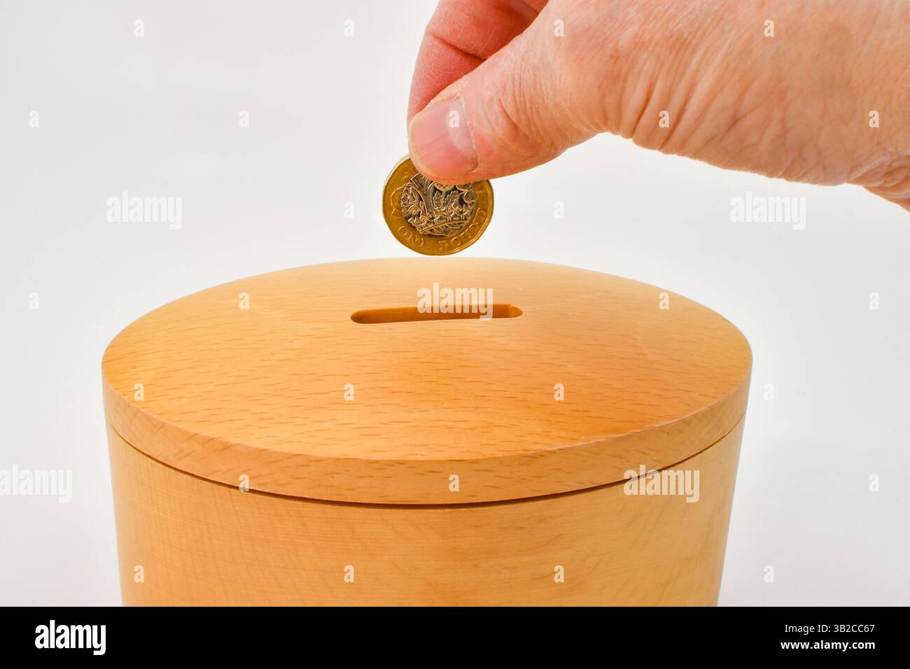Una moneta da una sterlina inserita nella fessura di una cassetta di legno . Concetto di salvataggio. Foto Stock