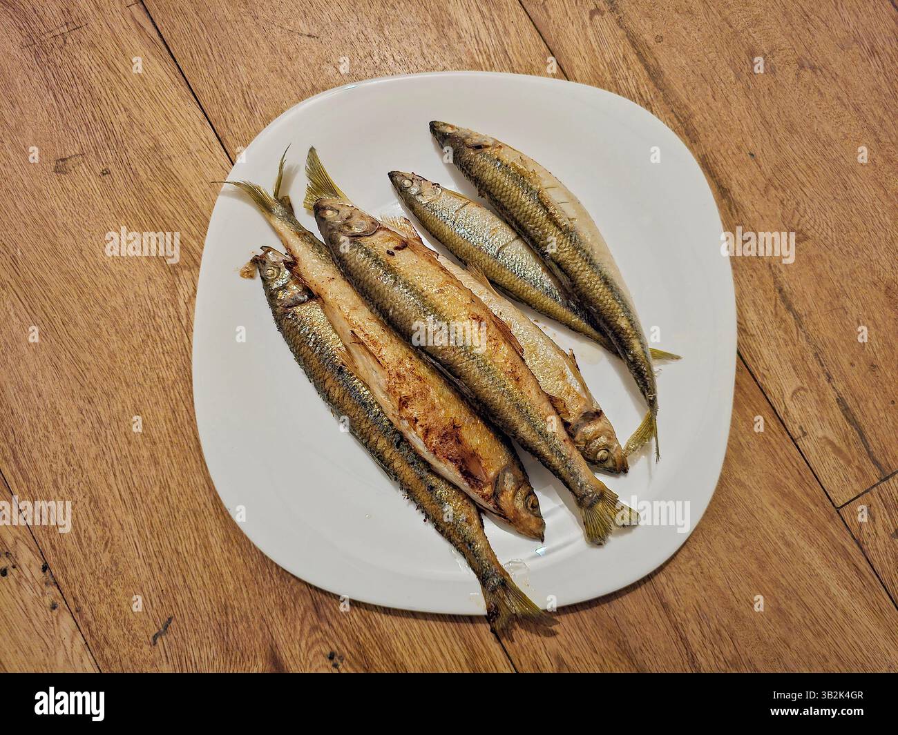Una vista ravvicinata di una deliziosa purea artica, fritta alla perfezione con pelle dorata, posizionata su un piatto bianco seduto su un rustico tavolo in legno Foto Stock