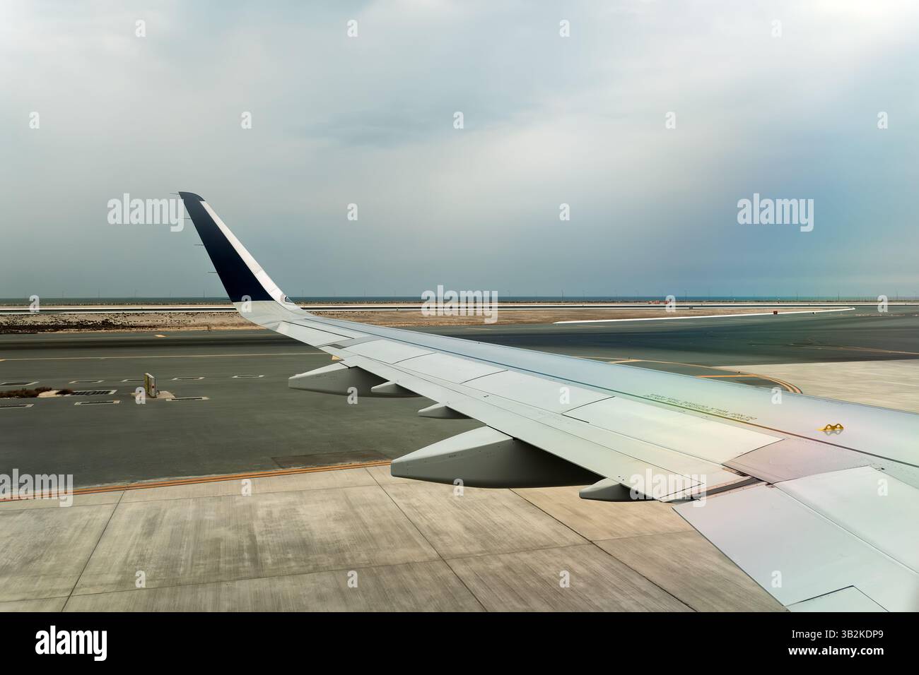 Un'ala di aeroplano fotografata durante l'atterraggio o il decollo in una giornata nuvolosa, che mostra il tempo coperto e l'ambiente umido della pista. Foto Stock