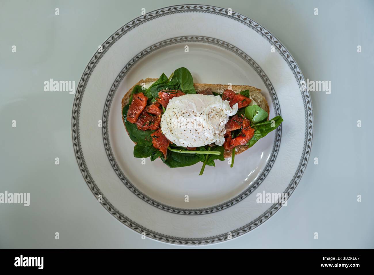 una deliziosa colazione con uova in camicia su una fetta di ciabatta con spinaci e pezzetti di pesce rosso salato Foto Stock