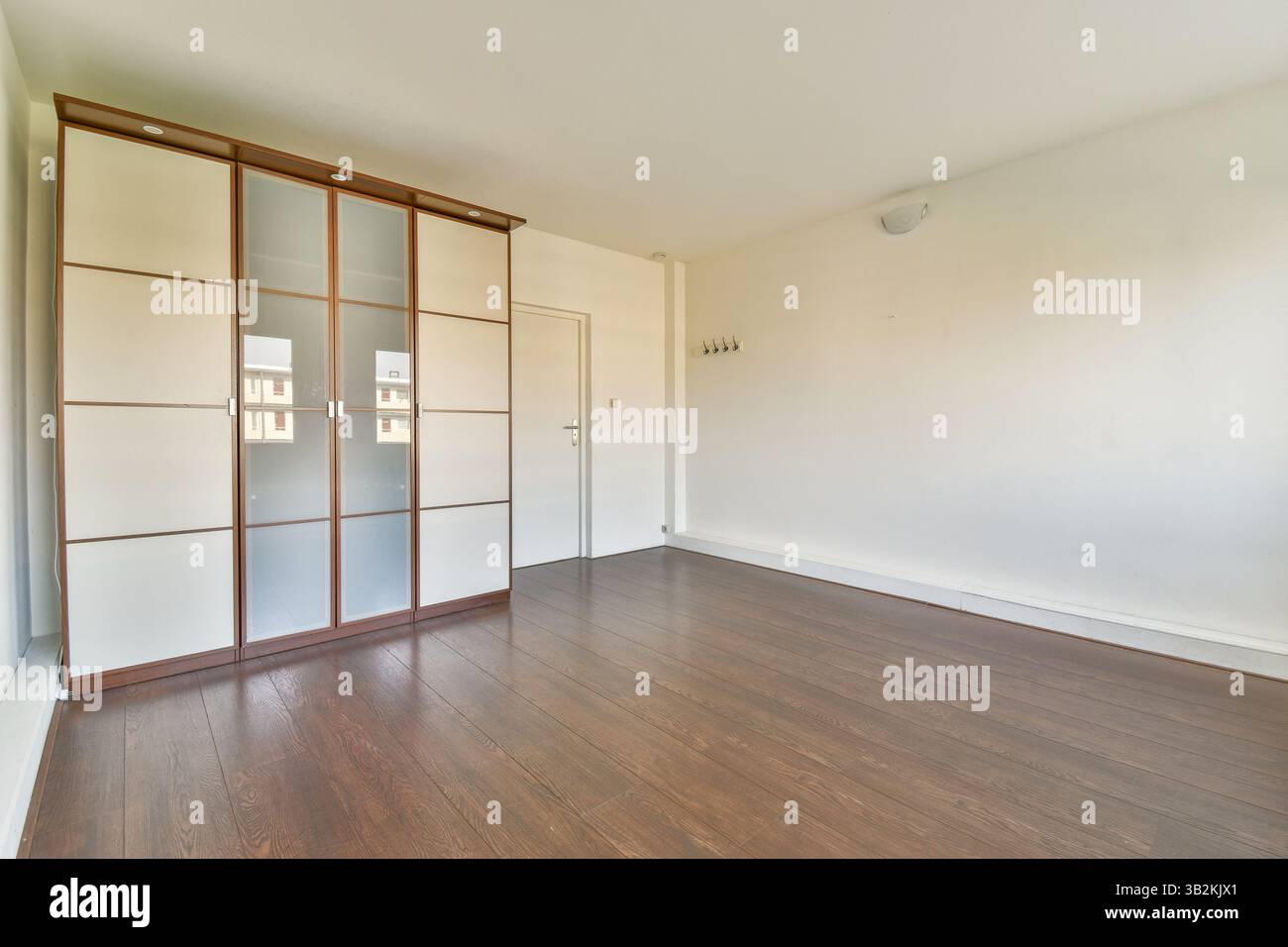 Camera luminosa e spaziosa con armadietto moderno, eleganti elementi di design e pavimento in legno lucido, perfetta per un soggiorno moderno. Foto Stock