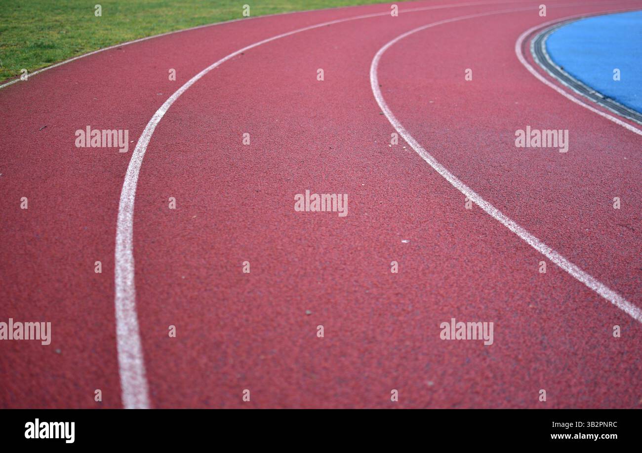 Curva rossa della pista da corsa con erba verde sul lato sinistro. Foto Stock