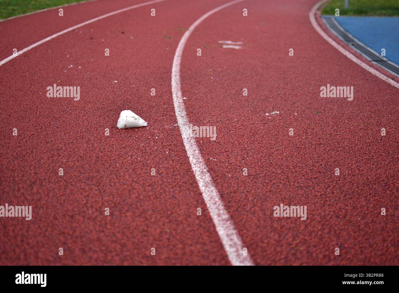 Curva rossa della pista da running con un pezzo di ghiaccio fangoso in inverno Foto Stock