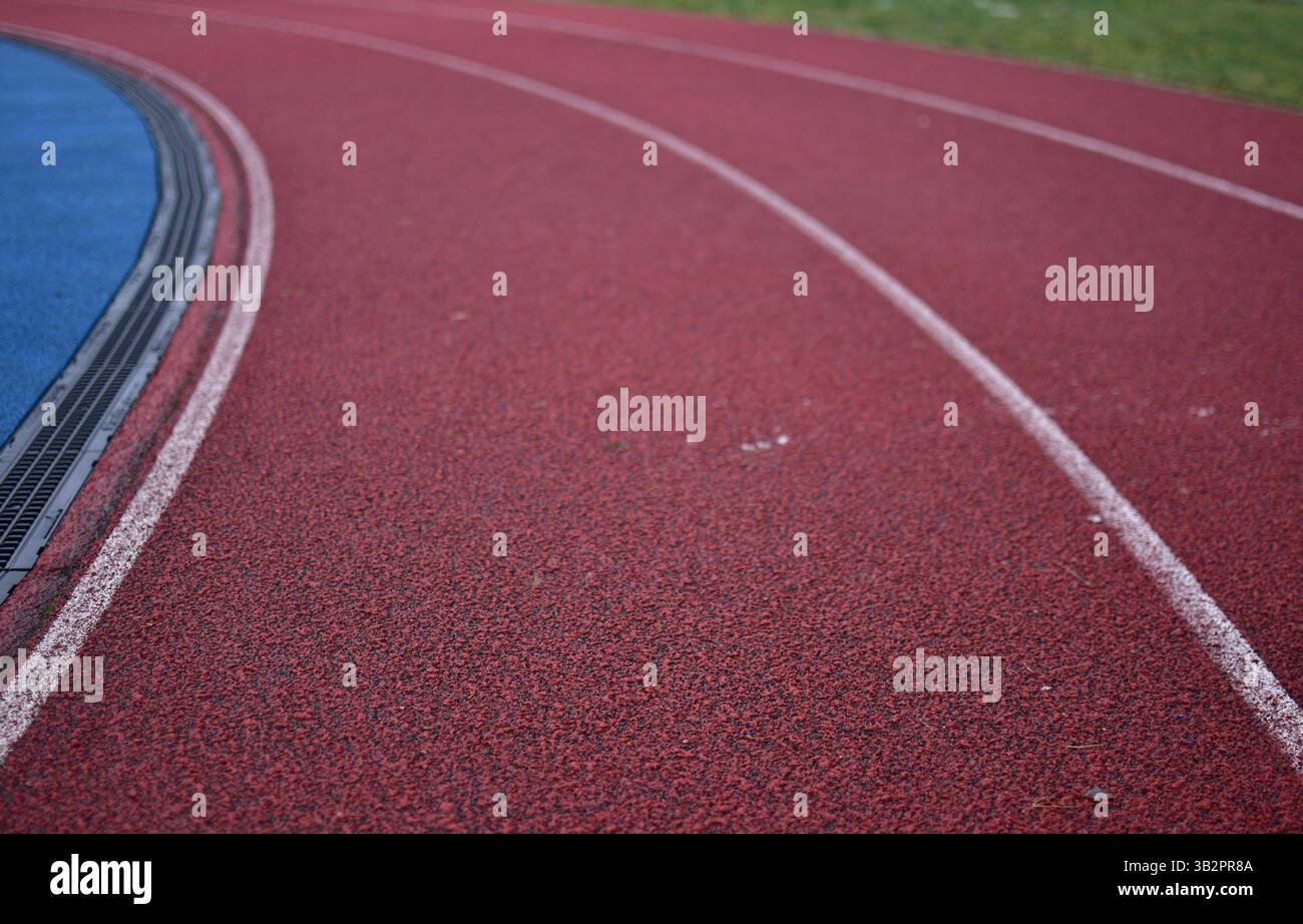 Curva rossa della pista da corsa con campo sportivo blu sul lato sinistro e erba verde sul lato destro. Foto Stock