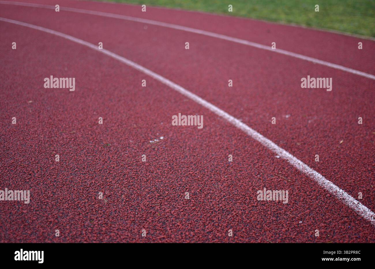Curva rossa della pista da corsa con erba verde sul lato destro. Foto Stock
