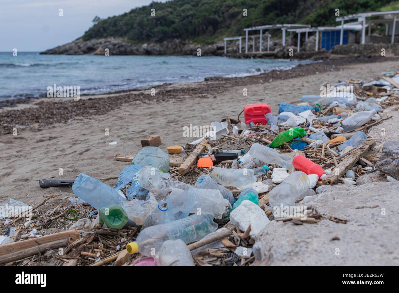 Primo piano di bottiglie di plastica e detriti di legno sulla spiaggia inquinata Foto Stock