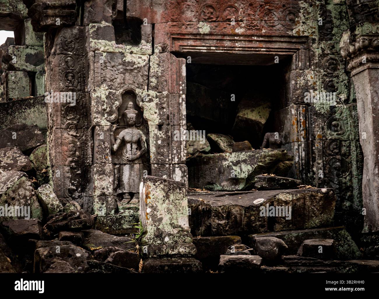 Antiche rovine in pietra con intricate incisioni, con una figura in abbigliamento tradizionale. La struttura mostra segni di agenti atmosferici e degrado, circondato da b Foto Stock