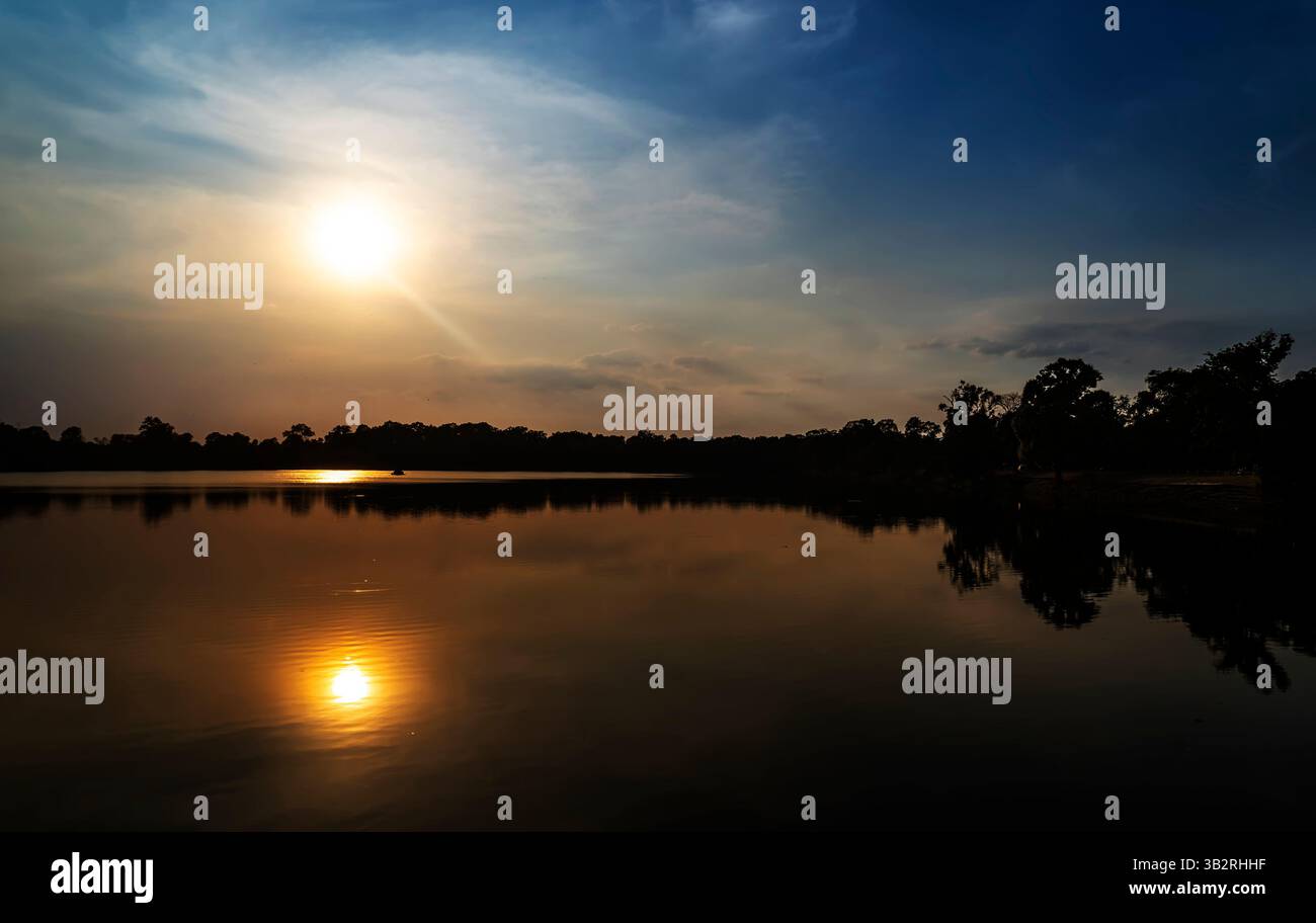 Un tramonto sereno su un lago calmo, con il sole che si riflette sulla superficie dell'acqua. Sagome di alberi fiancheggiano la riva, creando un'atmosfera tranquilla. Foto Stock