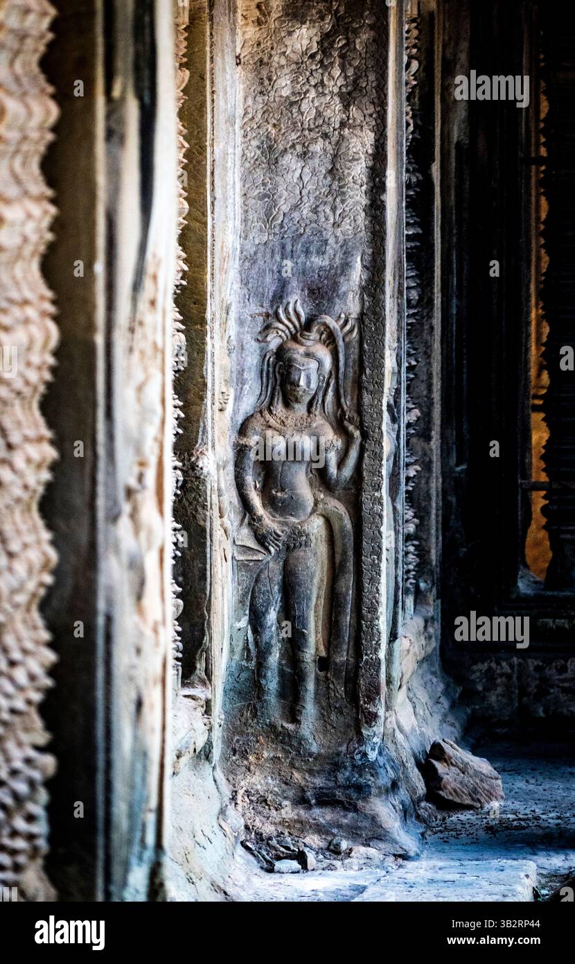 Una dettagliata scultura in pietra di una figura seduta, forse una divinità, posta contro un antico muro. Le texture e le ombre intricate mettono in risalto l'artigiano Foto Stock