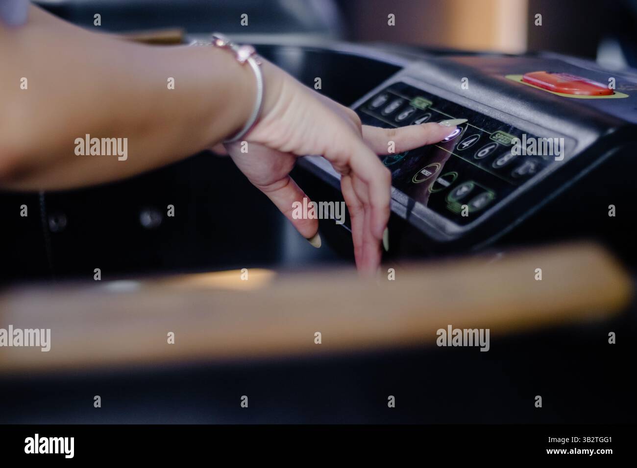 Un primo piano mostra la mano di una donna che regola la velocità su un tapis roulant, indicando un focus sulla forma fisica, le routine sane e l'integrazione tecnologica in Foto Stock