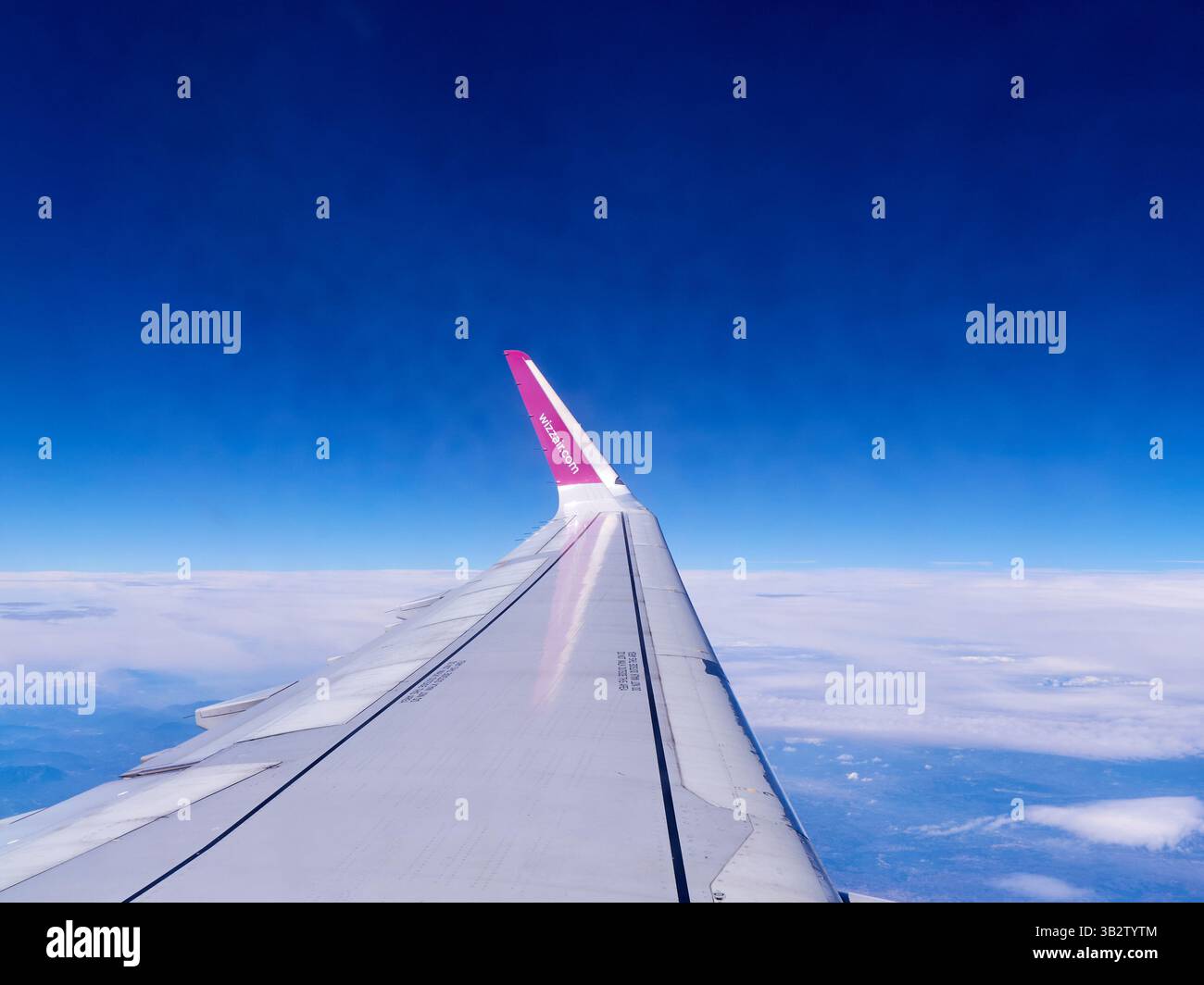 Ala dell'aereo Wizzair che vola nel cielo blu con nuvole bianche Foto Stock