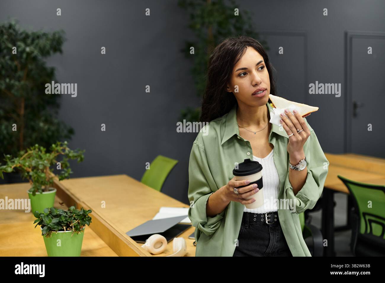 Un giovane professionista si prende un momento per assaporare cibo e bevande in uno spazio di lavoro contemporaneo. Foto Stock