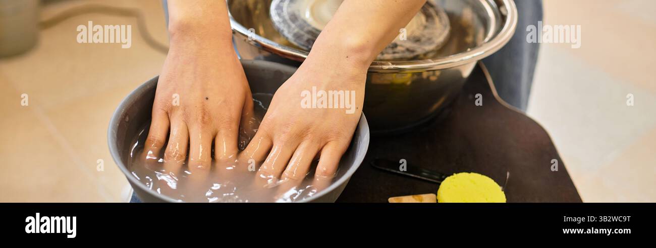 Le mani modellano sapientemente l'argilla in un vivace studio di ceramica, circondato da strumenti e materiali artistici. Foto Stock