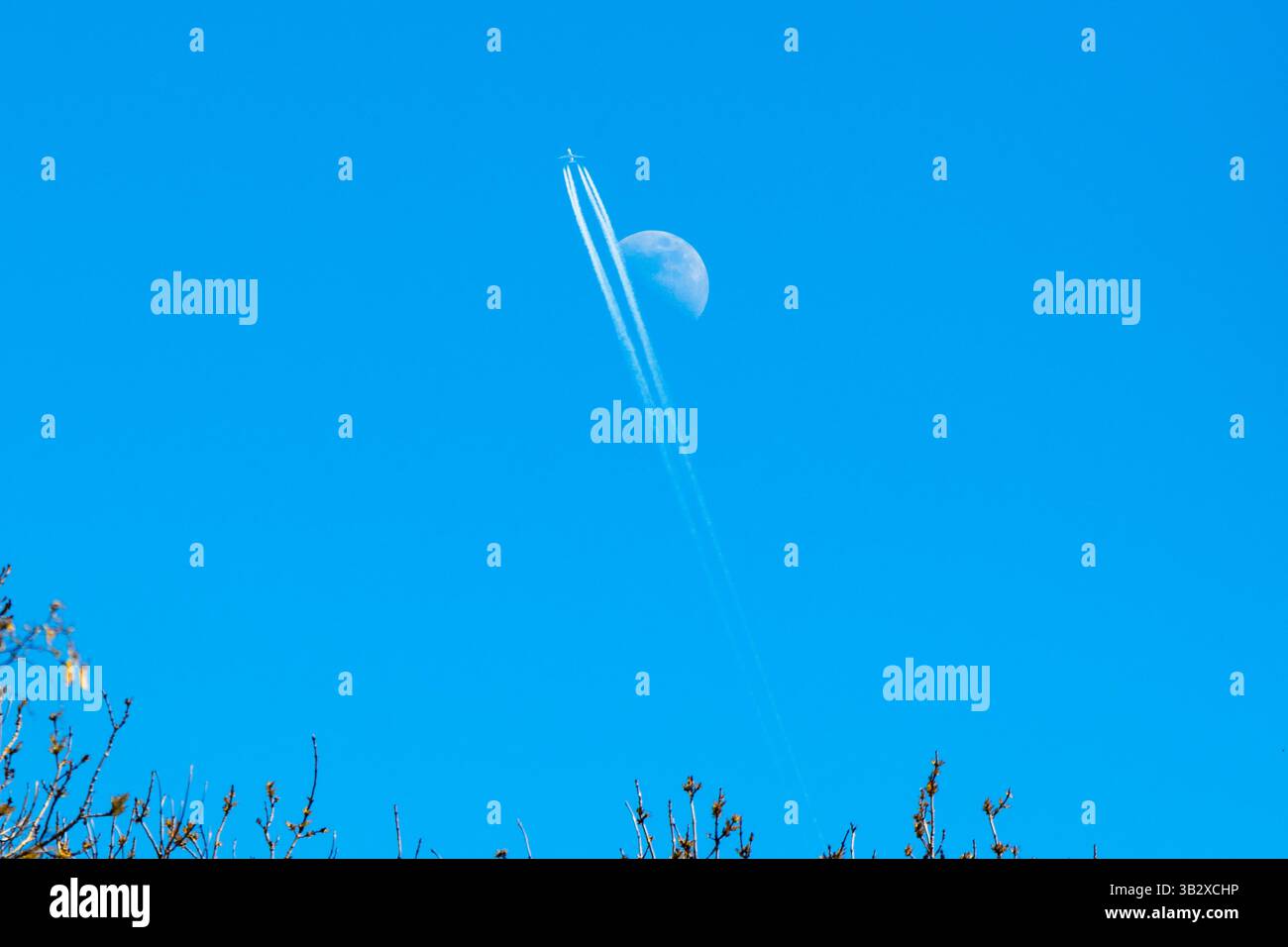 Un aereo in contrail passa il primo quarto di luna (4/5/25) in un cielo blu pomeridiano, Londra, Regno Unito Foto Stock