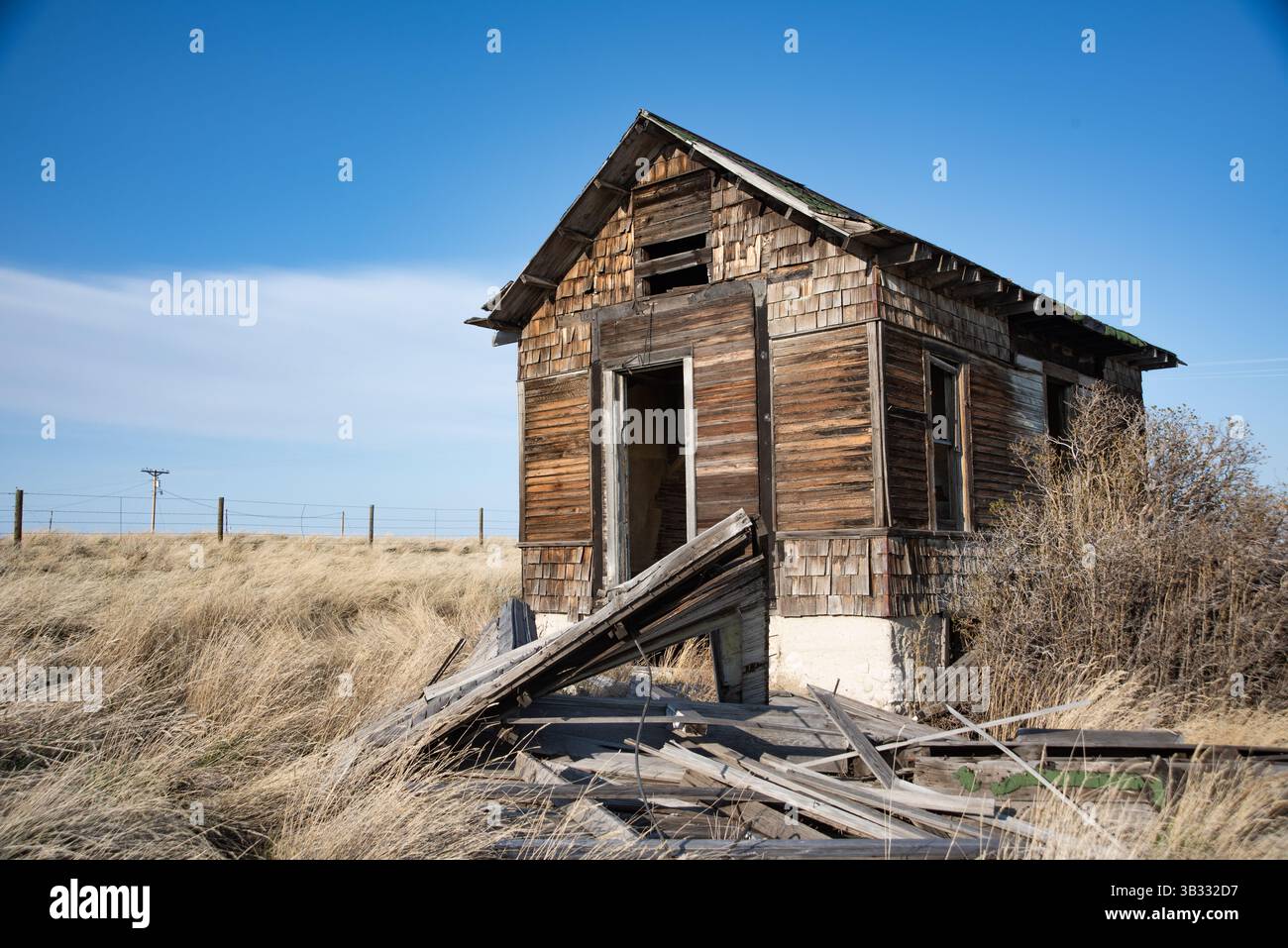 Una casa in legno abbandonata si trova in un campo erboso nel Wyoming rurale, mostrando segni di decadenza e abbandono con finestre rotte e una struttura cedevole. Foto Stock
