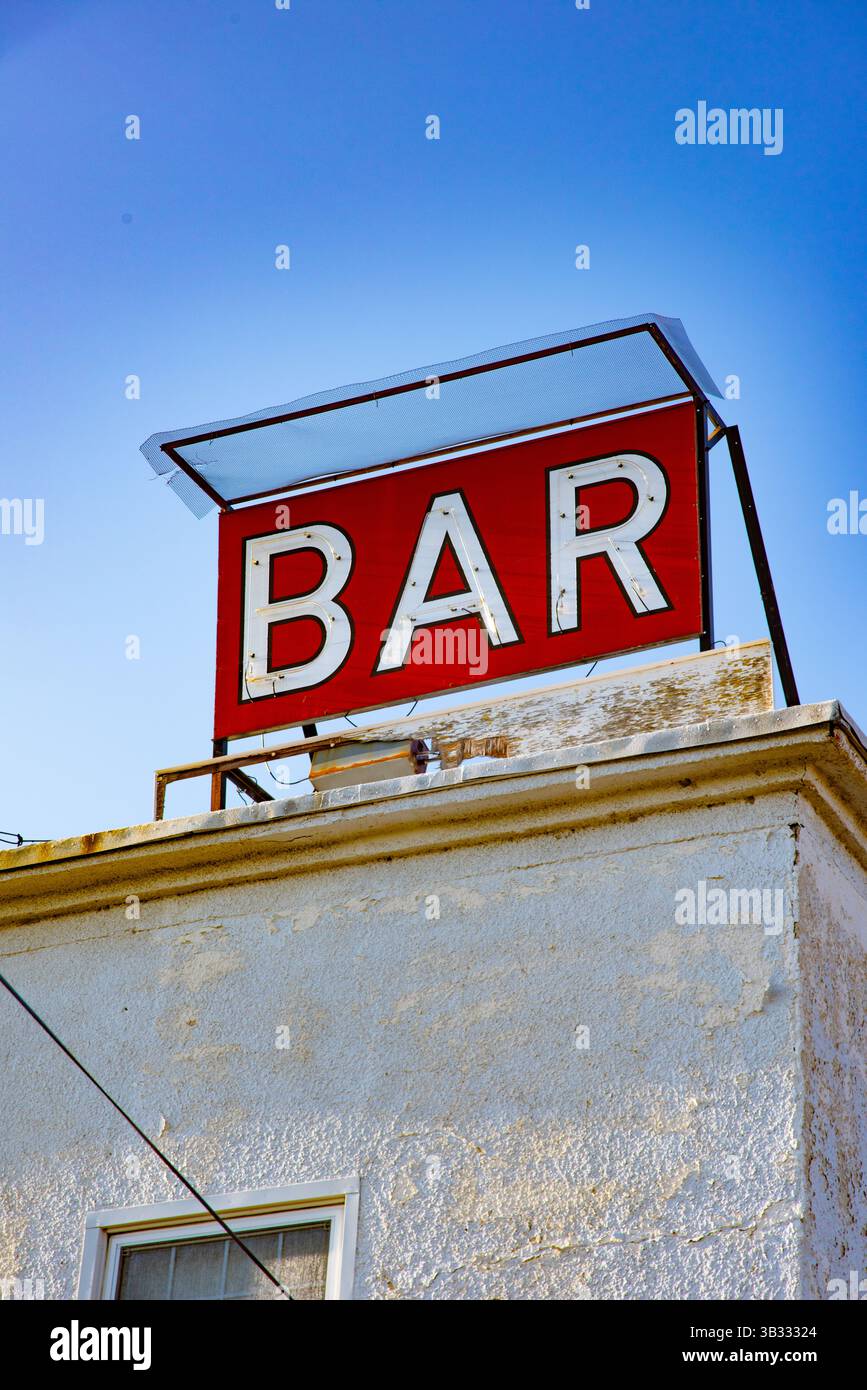 Un'insegna rossa da bar d'epoca si trova in una tranquilla zona rurale del Wyoming occidentale, vista contro un cielo azzurro. Foto Stock