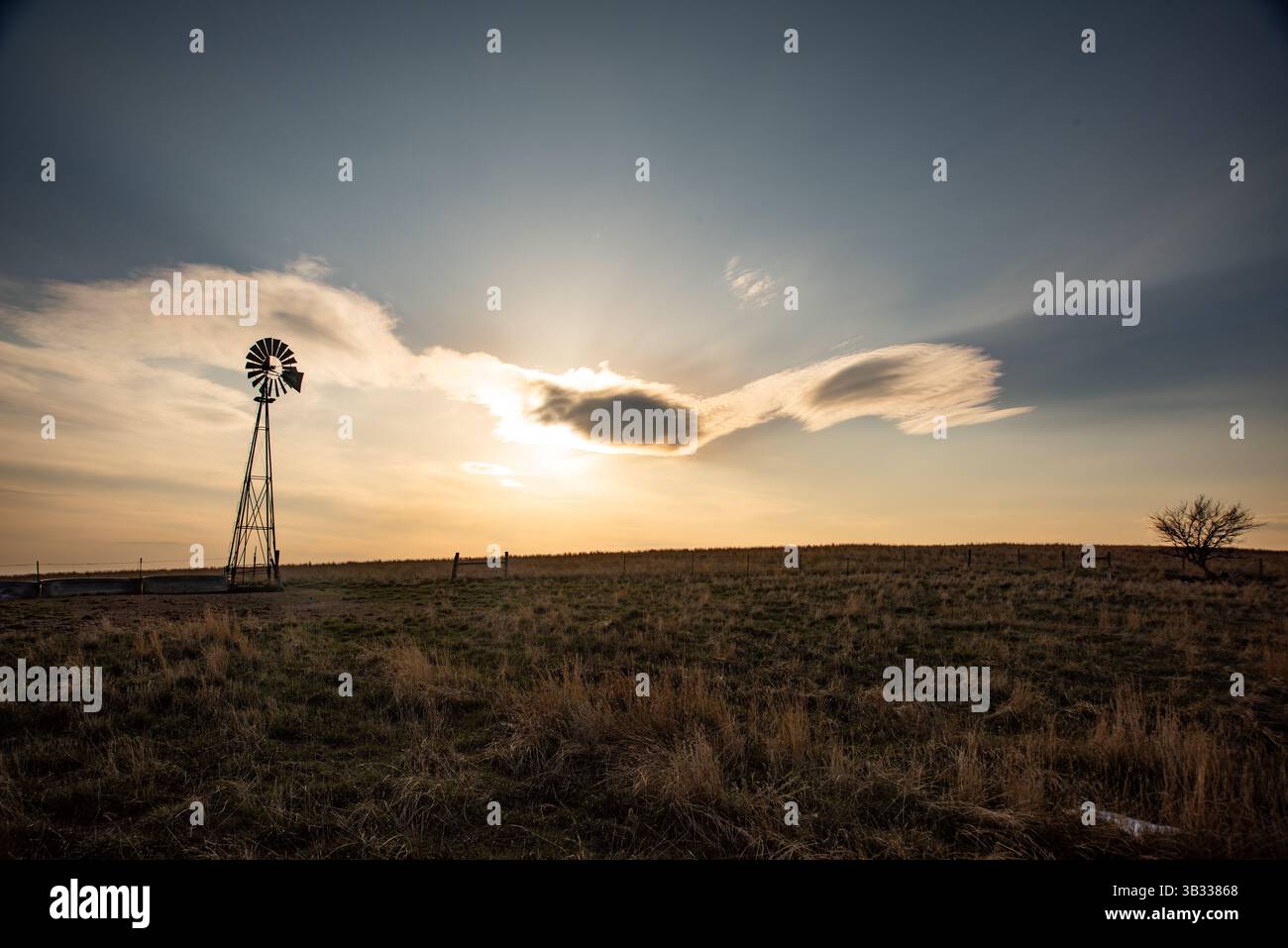In un tranquillo paesaggio rurale del Wyoming occidentale, un antico mulino a vento si erge sullo sfondo di uno splendido tramonto. Foto Stock