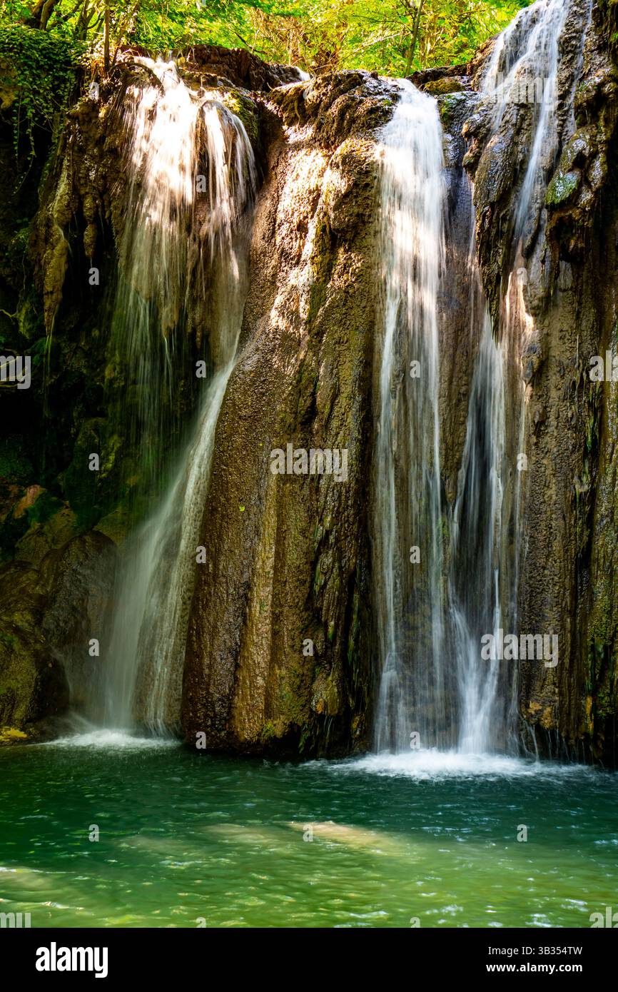 Una cascata mozzafiato scorre graziosamente in una tranquilla piscina, circondata da una vegetazione vibrante e da alberi baciati dal sole Foto Stock