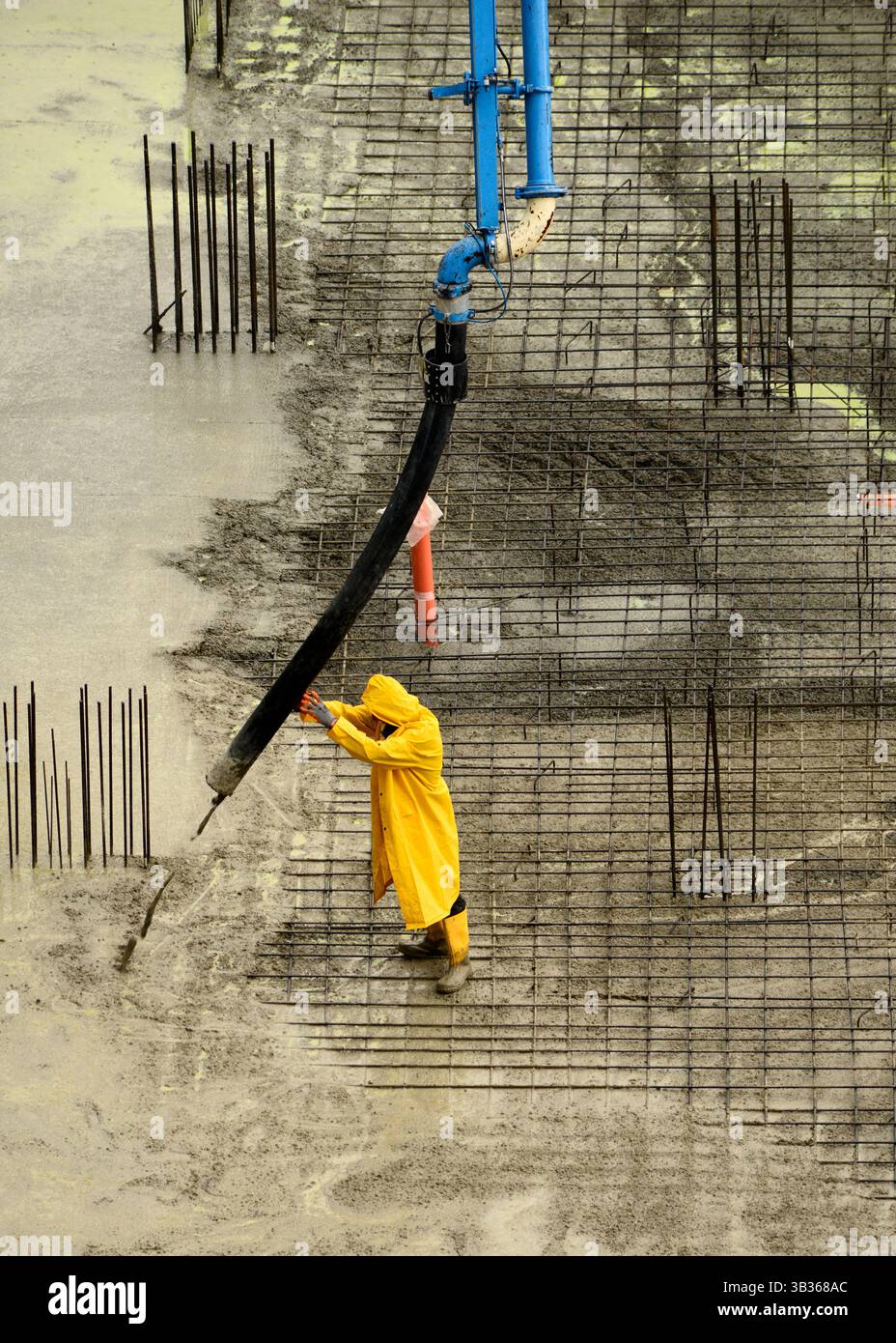 Operaio edile che gestisce il flusso di calcestruzzo dalla pompa durante i lavori di fondazione in un cantiere edile. Lavoro manuale nel settore delle costruzioni. Foto Stock