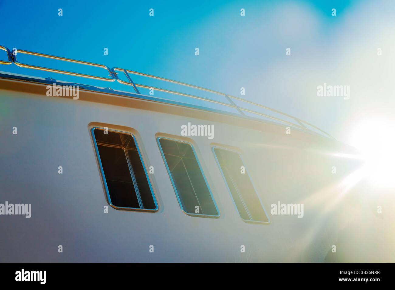 Lo scafo di un lussuoso yacht bianco a motore, con oblò sopra, contro il cielo blu e la luce del sole nell'angolo, vista dal basso. Foto Stock