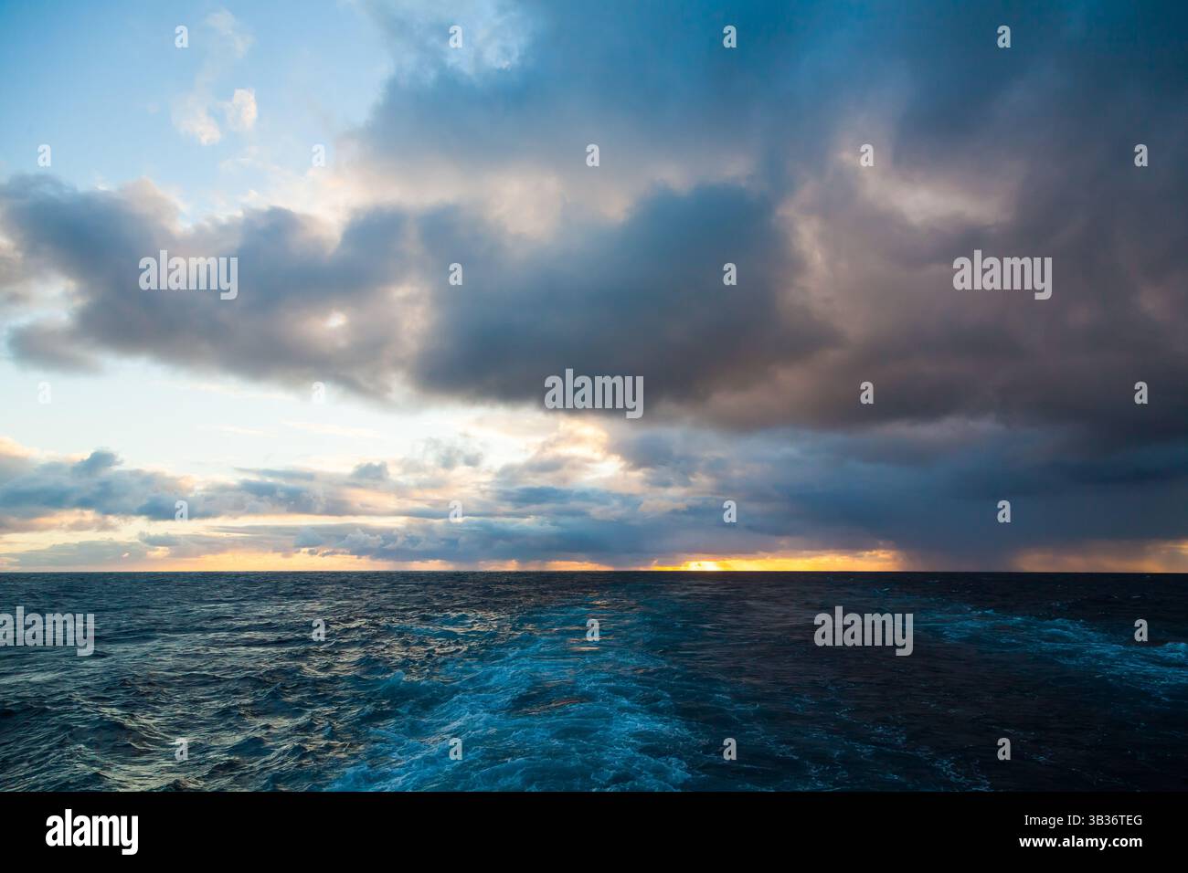 Cielo al tramonto con raggi di luce da sotto le nuvole nell'oceano e tracce sull'acqua dal movimento della nave. Foto Stock