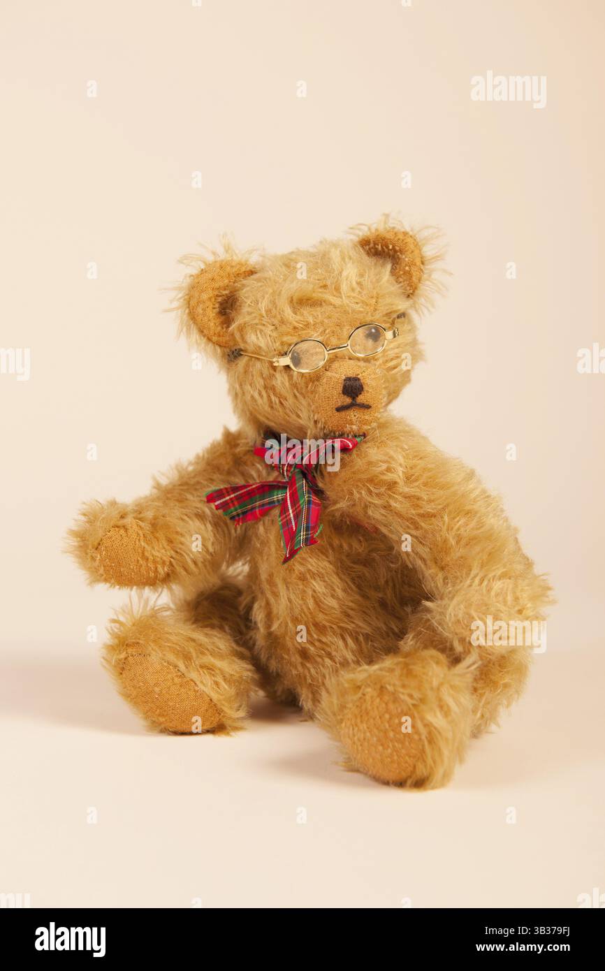 Farcite orso vintage con gli occhiali seduto su sfondo beige Foto Stock