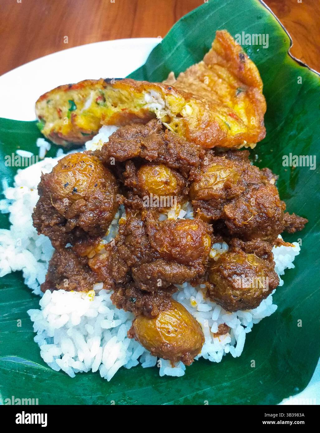Rendang Kentang o Rendang Potatoes, un piatto di Minangkabau Padang di Sumatra occidentale servito su riso bianco con omelette su una foglia di banana per il takeaway. Foto Stock